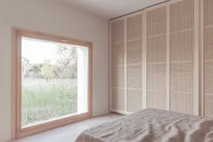 A bedroom with wooden walls and a large window overlooking a grassy field.
