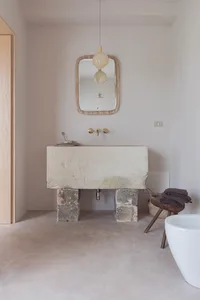 A minimalist bathroom with a concrete floating sink, white bathtub, and wooden stool with towels.
