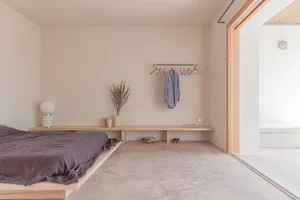 A minimalist bedroom with a concrete floor and a low wooden bed platform.