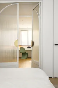 A minimalist bedroom with glass doors and a green chair.
