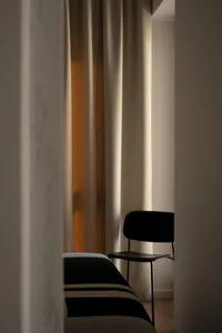 A minimalist bedroom featuring a black chair, a bed with white and black striped bedding, and sheer curtains letting in soft