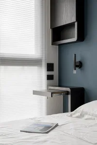 A minimalist bedroom featuring a wooden desk, blinds, and a comfortable bed with white bedding.