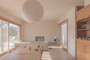 A minimalist living room featuring a concrete floor, large windows, and a wooden cabinet.