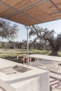 Minimalist outdoor cooking area with concrete countertops, brass faucets, and a view of olive trees.
