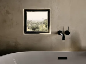 A modern bathroom featuring a concrete window overlooking an urban landscape, with a black wall-mounted tap.