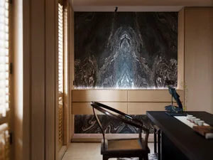 Modern living room featuring marble walls and wooden furniture with a black table and chair.
