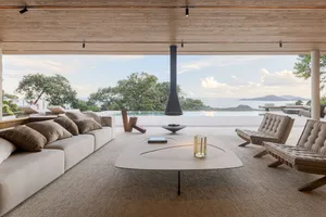 Contemporary minimalist living room with white leather sofas and a glass fireplace on a wooden patio overlooking the ocean.
