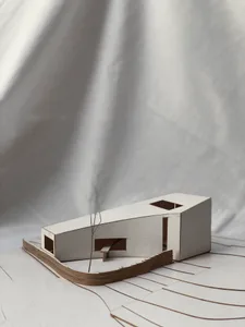 A modern residential building model crafted from cardboard materials on a white surface with floor plan layout lines.