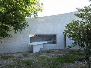 Modern residential home made of concrete with large windows and outdoor area.