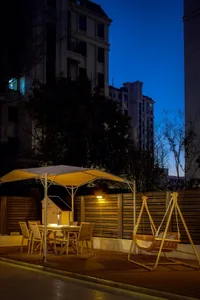 A modern residential patio with a wooden table, chairs, a hanging swing, and warm lighting, surrounded by a wooden fence and 