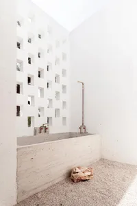 A minimalist industrial-style bathroom with concrete walls and floors, featuring a walk-in shower and a rock-like object on t