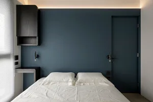 A minimalist bedroom with white bedding, dark wooden walls, and a sleek, modern design.