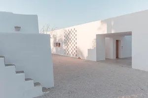 White concrete residential entry with a small stone staircase and a patterned window.