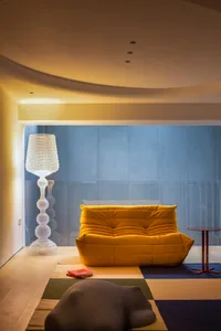 A modern lounge space featuring a yellow sofa, a tall white floor lamp, and a colorful rug.