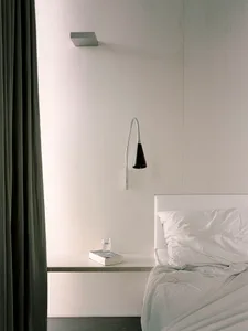 A minimalist bedroom with a white bed and grey curtains, featuring a white nightstand, a fabric lampshade, and a glass water