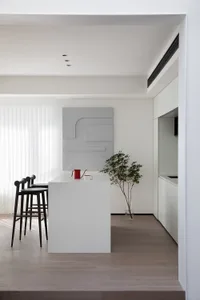 A minimalist residential kitchen with white surfaces and black stools.