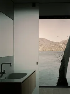 Minimalist bathroom with concrete countertop and large window overlooking a body of water.