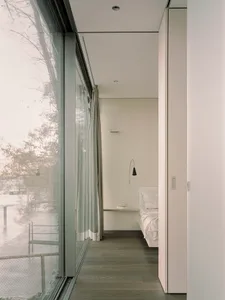 Modern minimalist bedroom with glass window, white walls, and wooden floor.