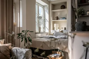 A minimalist bedroom featuring neutral-toned fabrics, light-colored wood, and plants