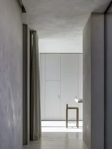 Minimalist white interior with concrete walls and floor, viewed through a narrow corridor.