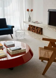 Photograph of a minimalist living room with a terrazzo floor and a sleek, rounded red coffee table.