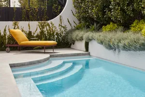 Minimalist poolside seating area with a concrete platform and yellow fabric lounge chair.