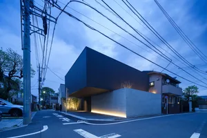 A modern, single-story concrete house with a black wall and white brick accents, illuminated by ambient lighting at dusk.