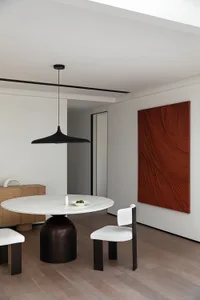 A modern dining room with a round marble table, white chairs, and a black pendant light.