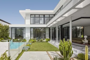 Modern residential house featuring concrete and glass materials with a large swimming pool and a well-manicured lawn.