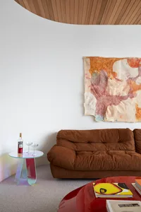 Contemporary living room featuring a brown fabric sofa, abstract artwork, and a sleek side table with a bottle of Campari and
