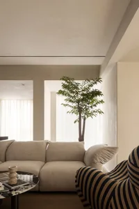 A modern living room with a neutral color palette, featuring a beige sectional sofa, a black and white striped armchair, and 