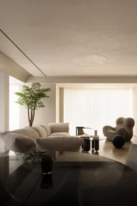 Modern living room featuring wooden floor, glass coffee table, fabric sofa, and potted plant.