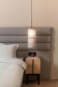 A modern minimalist bedroom featuring a textured headboard with a hanging pendant light above a side table.