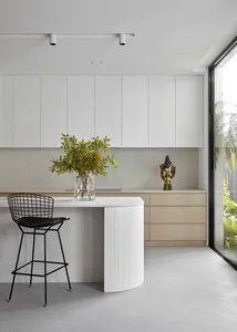 Modern minimalist kitchen with concrete countertops, white cabinets, and a black wire-frame barstool.
