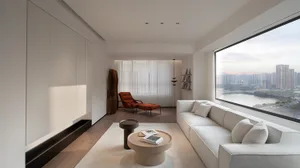 Contemporary living room with a minimalist design, featuring a white sofa, a round coffee table, and a large window with city