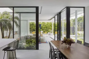 A minimalist living room with glass walls and concrete floor, showcasing sleek design and natural light.