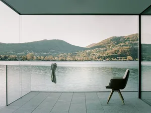 Modern residential interior with floor-to-ceiling glass walls overlooking a serene lake and mountains.