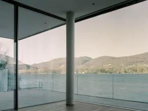 Modern residential interior featuring glass walls overlooking water and concrete columns