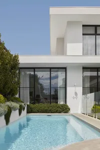 Modern minimalist two-story house with white stucco exterior and large glass windows.