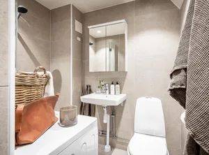 A minimalist bathroom with beige tiled walls, a white toilet, and a sink with a mirror above.