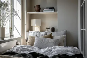 A minimalist bedroom with a bed featuring a mix of white and gray linens and decorative pillows, alongside ceramics and a del
