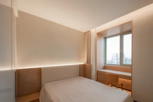 Minimalist bedroom with a white bed and wooden accents, featuring a window with a city view.