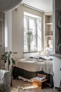 A minimalist bedroom with a wooden bed and window with white curtains.