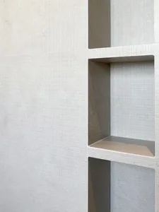 A minimalist design featuring a textured concrete wall with recessed shelves.