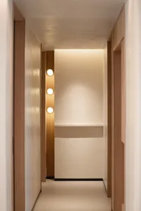 A minimalist corridor with wood panels and white painted walls, featuring round lighting fixtures.
