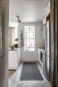 A minimalist kitchen with wooden flooring, featuring stainless steel appliances and a cozy, modern atmosphere.