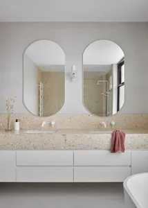 A modern bathroom featuring a terrazzo countertop with a double sink, white cabinets, and a freestanding tub in front of larg