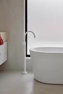 Modern minimalist bathroom featuring a white ceramic free-standing tub with a sleek, curved faucet next to a frosted window.
