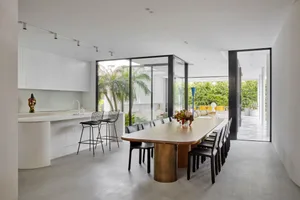 Modern dining room with transparent glass walls and a large wooden table surrounded by black chairs.