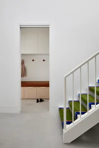 Staircase with green carpeted steps and white railings leading to an entryway with a bench and coat hooks.
